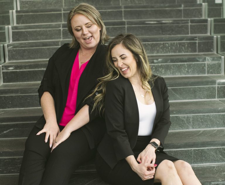 Two businesswomen sit on the stairs laughing